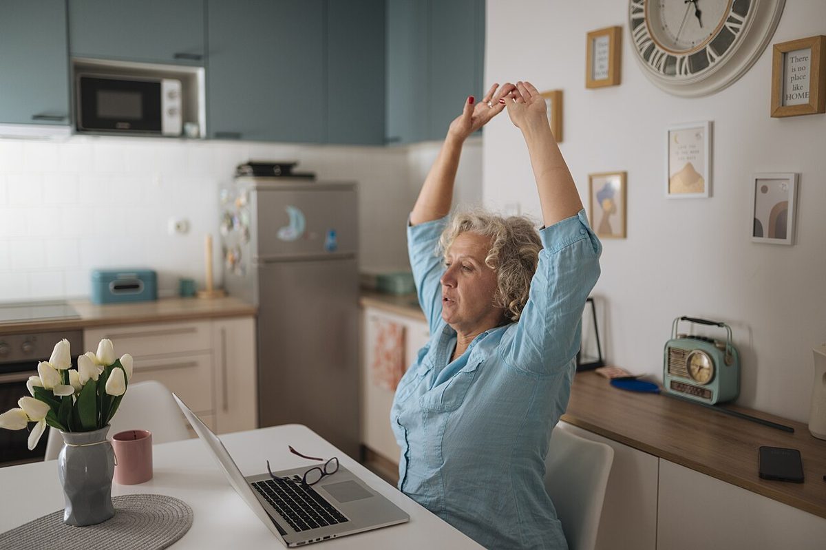 Woman stretching at a home office desk beside her laptop